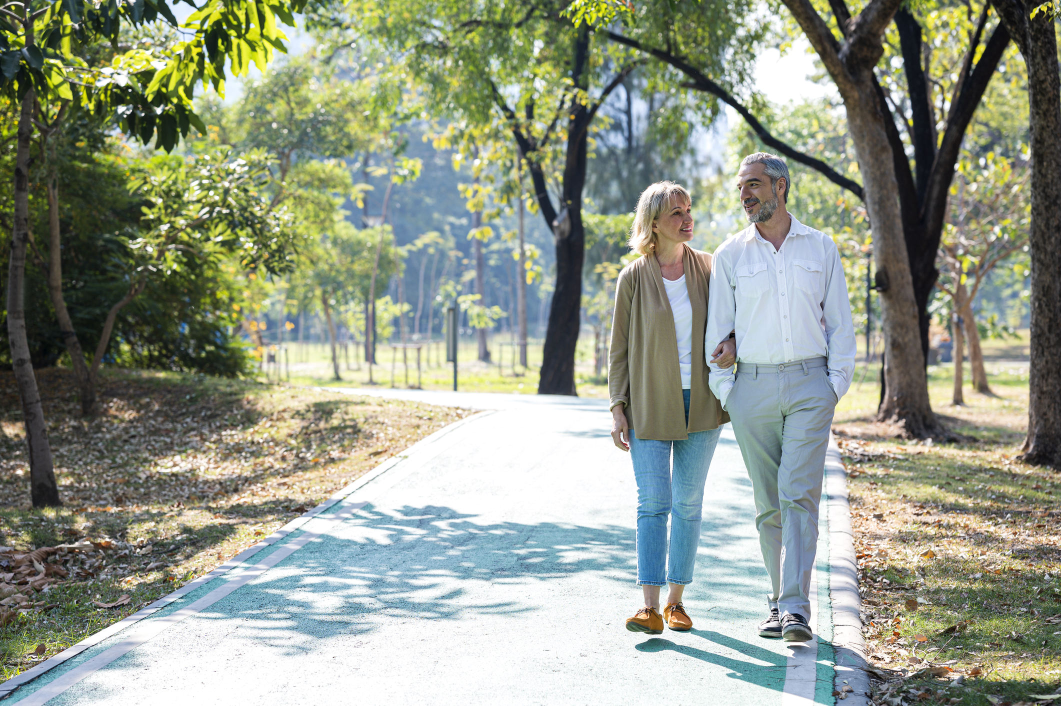 A middle aged couple takes a casual walk through a park.