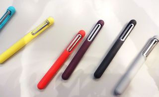 A variety of different colour pens with a silver clips on a white surface.