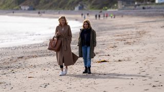 Rosaline (Eve Best) and Cathy (Stockard Channing) are walking along the beach and talking - Rosaline is carrying a large handbag.