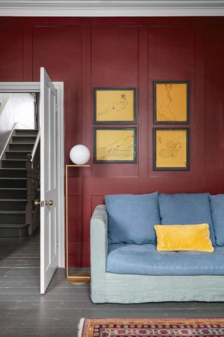 A living room with deep red walls and yellow artworks