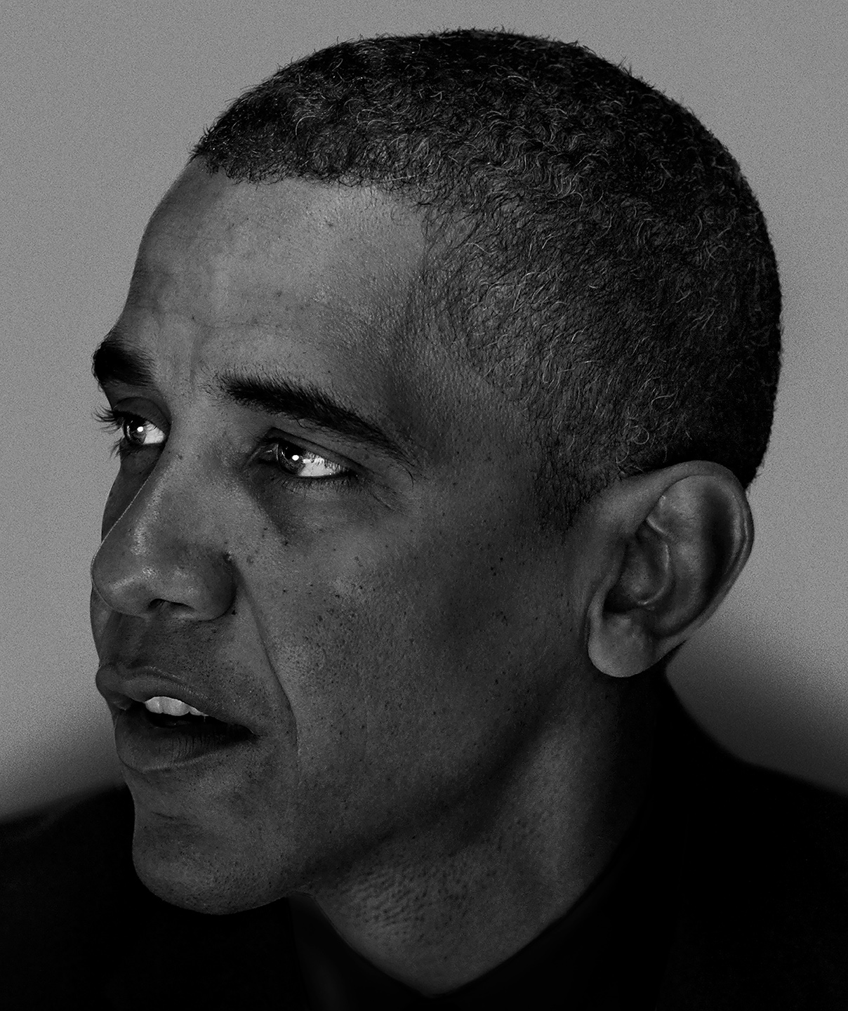 A close-up black-and-white portrait of Barack Obama, his eyes glancing to the left and his mouth slightly open as if mid-sentence, against a plain grey background.