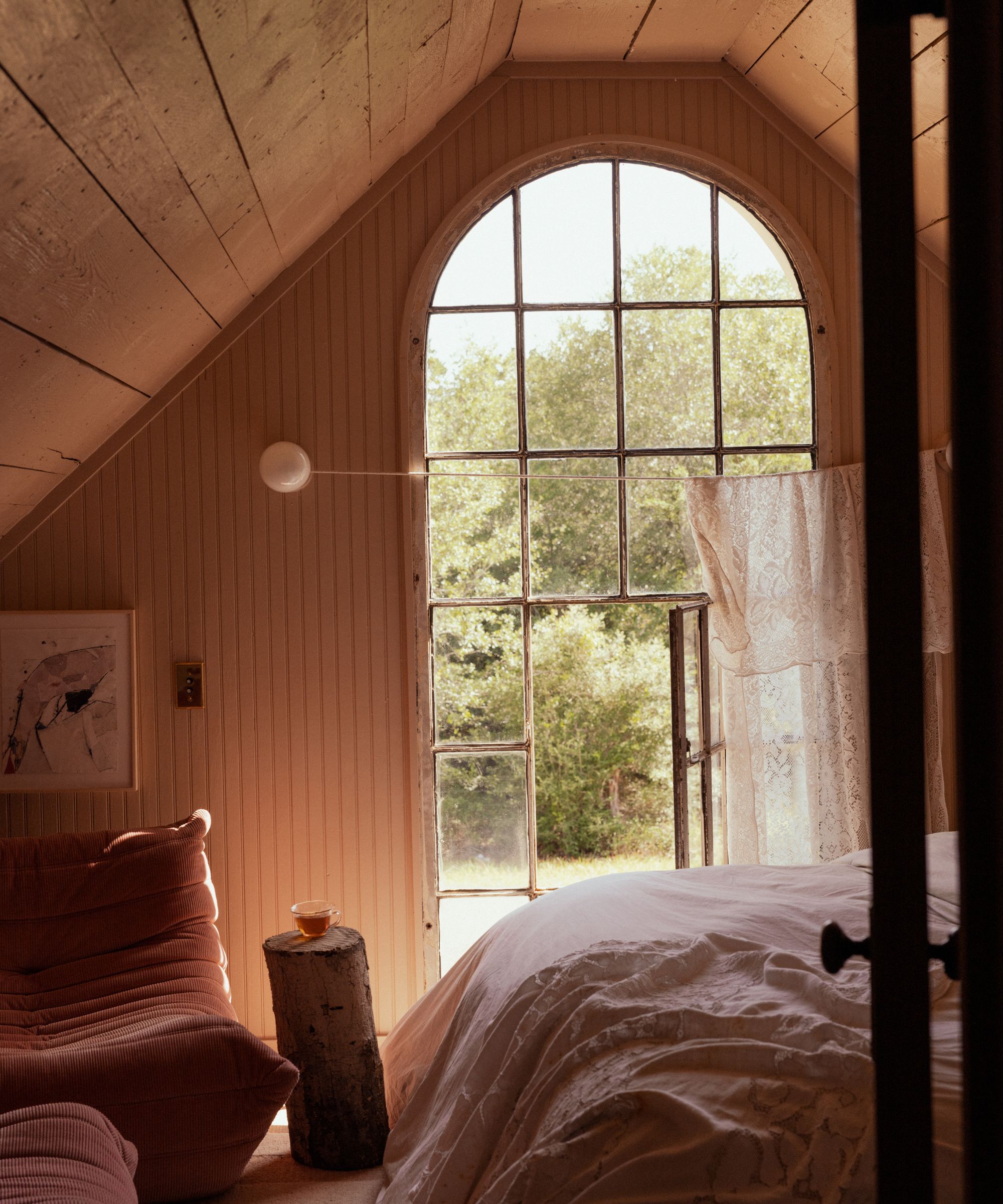 Bedroom with wood panelling, large arched window, togo chairs and lace curtain window treatment