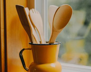 Wooden spoons and utensils in a yellow jar on a windowsill