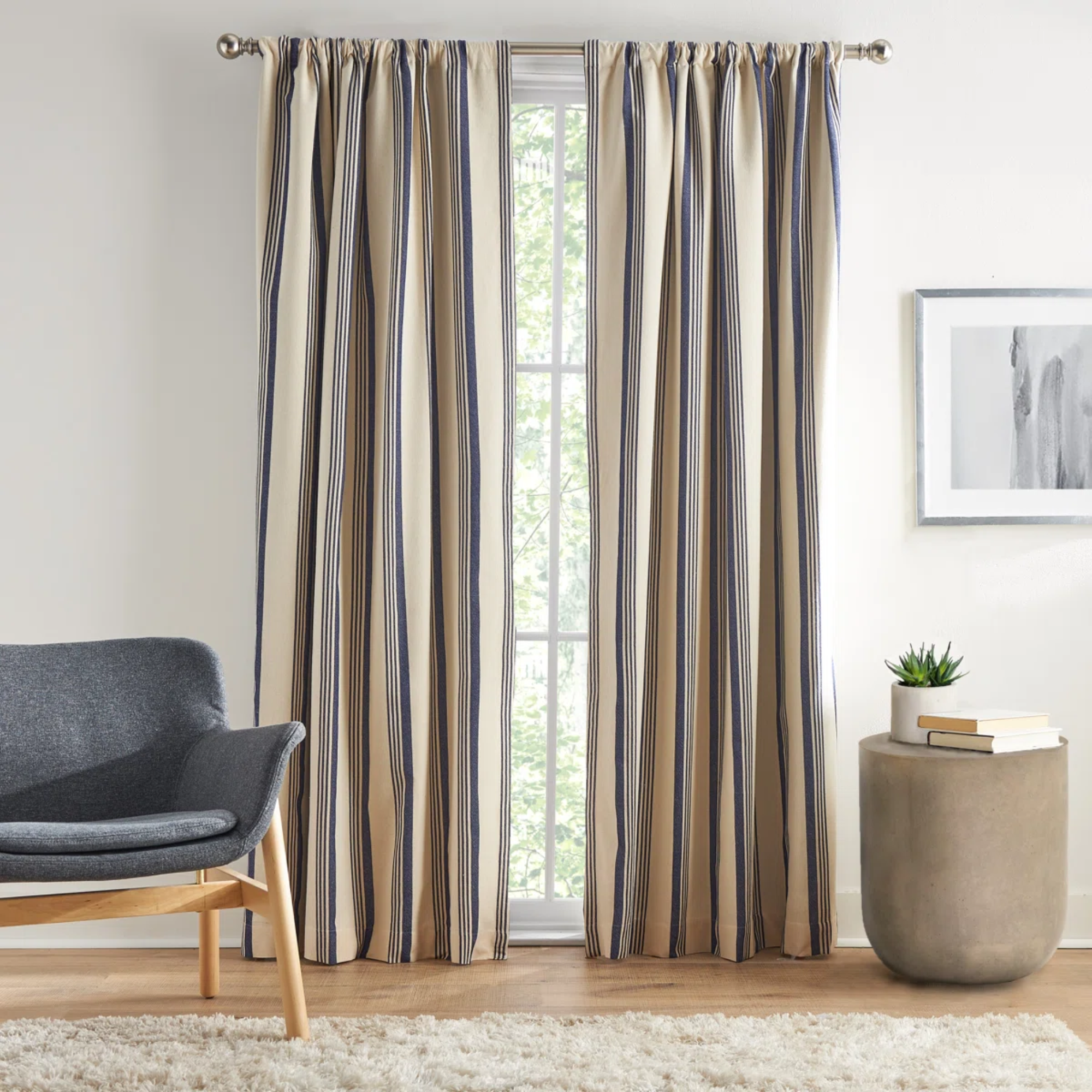 a room with a large window covered by striped curtains, an accent chair on the left and a side table on the right