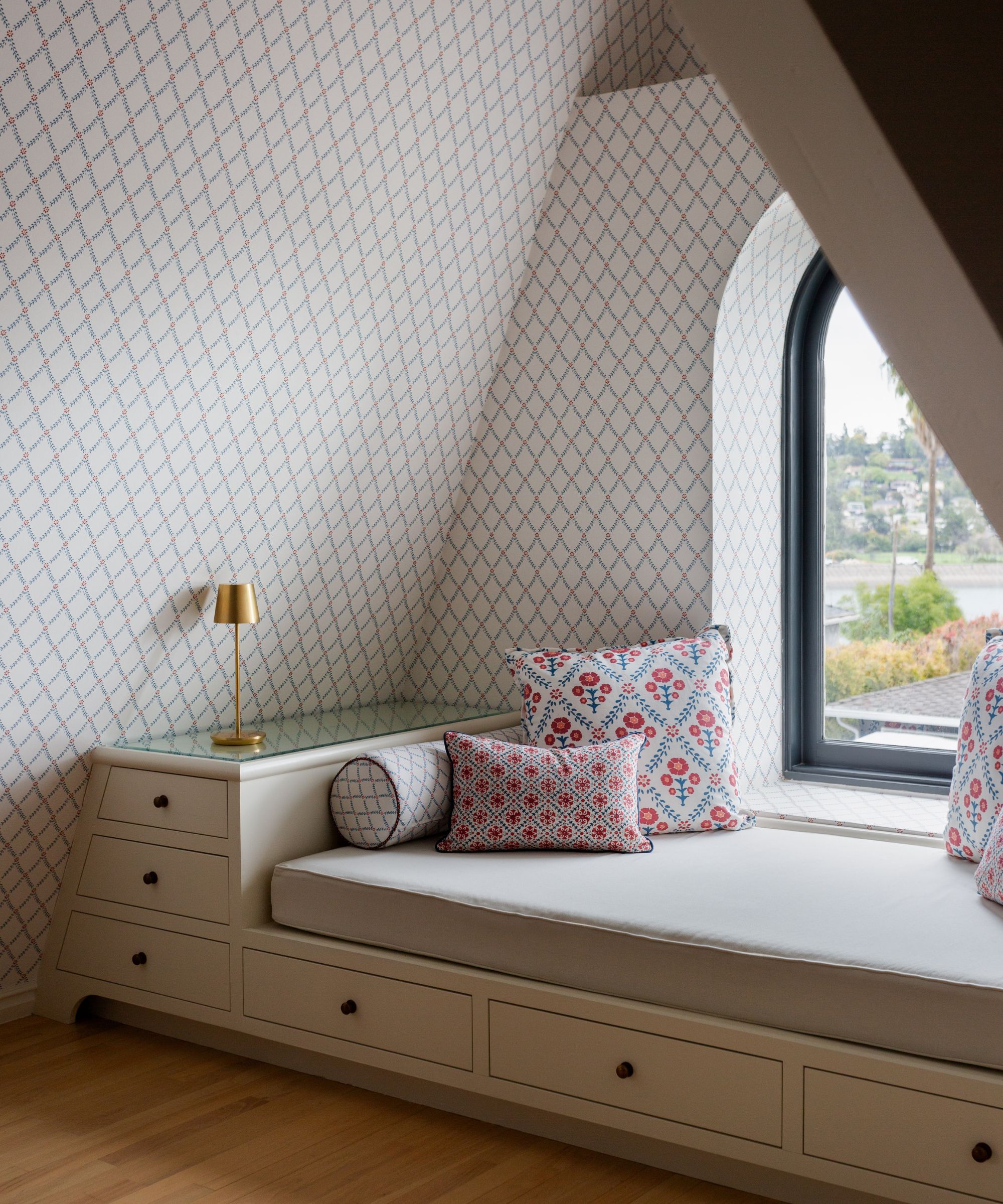a window seat daybed in LA with wallpapered walls and an arched window