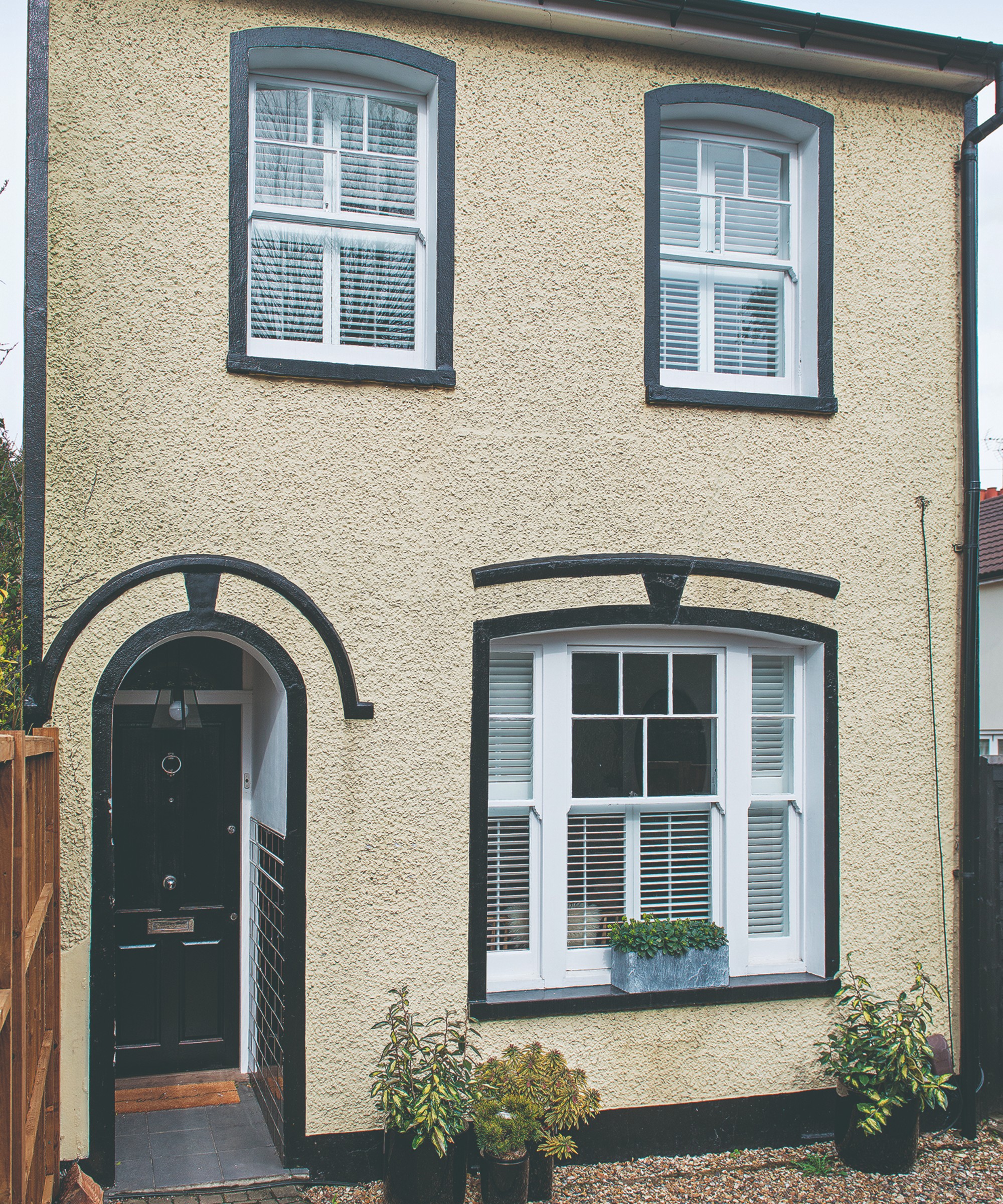 A beige-painted two-storey town house with a black front door with an arched porched