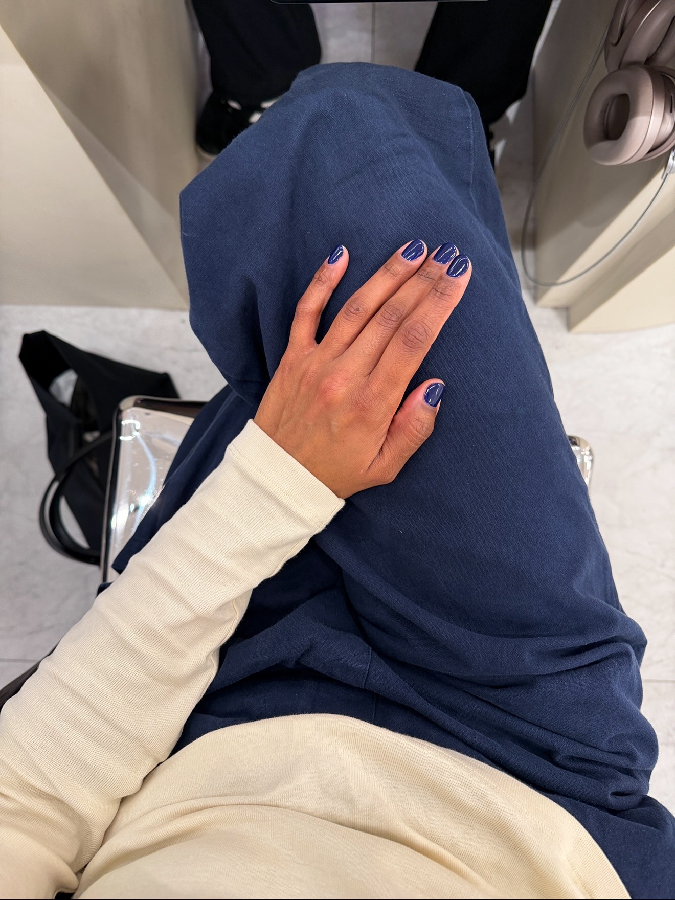 A woman taking a picture of her navy blue manicure, wearing matching blue trousers