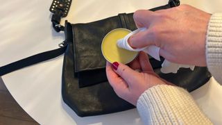 Someone using beeswax on a leather handbag on a white table