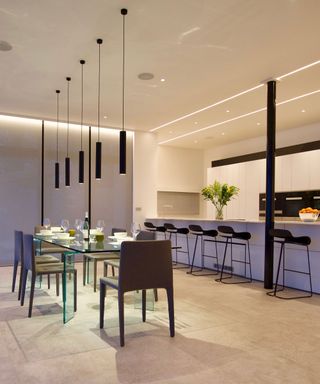 A large modern kitchen with a glass dining table and a white island nearby with black bar stools