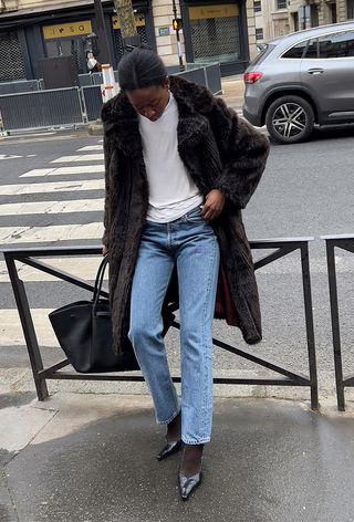 winter tight outfit shown in a photo of a woman wearing a fur coat over a white turtleneck with black tights layered under jeans styled with black pumps and a black bag