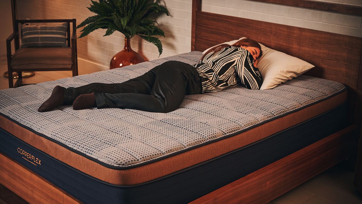 Our mattress tester in white and black silk pyjamas laying on her front on the Brooklyn Bedding Copperflex Memory Foam Mattress on wooden bed frame in sleep studio.
