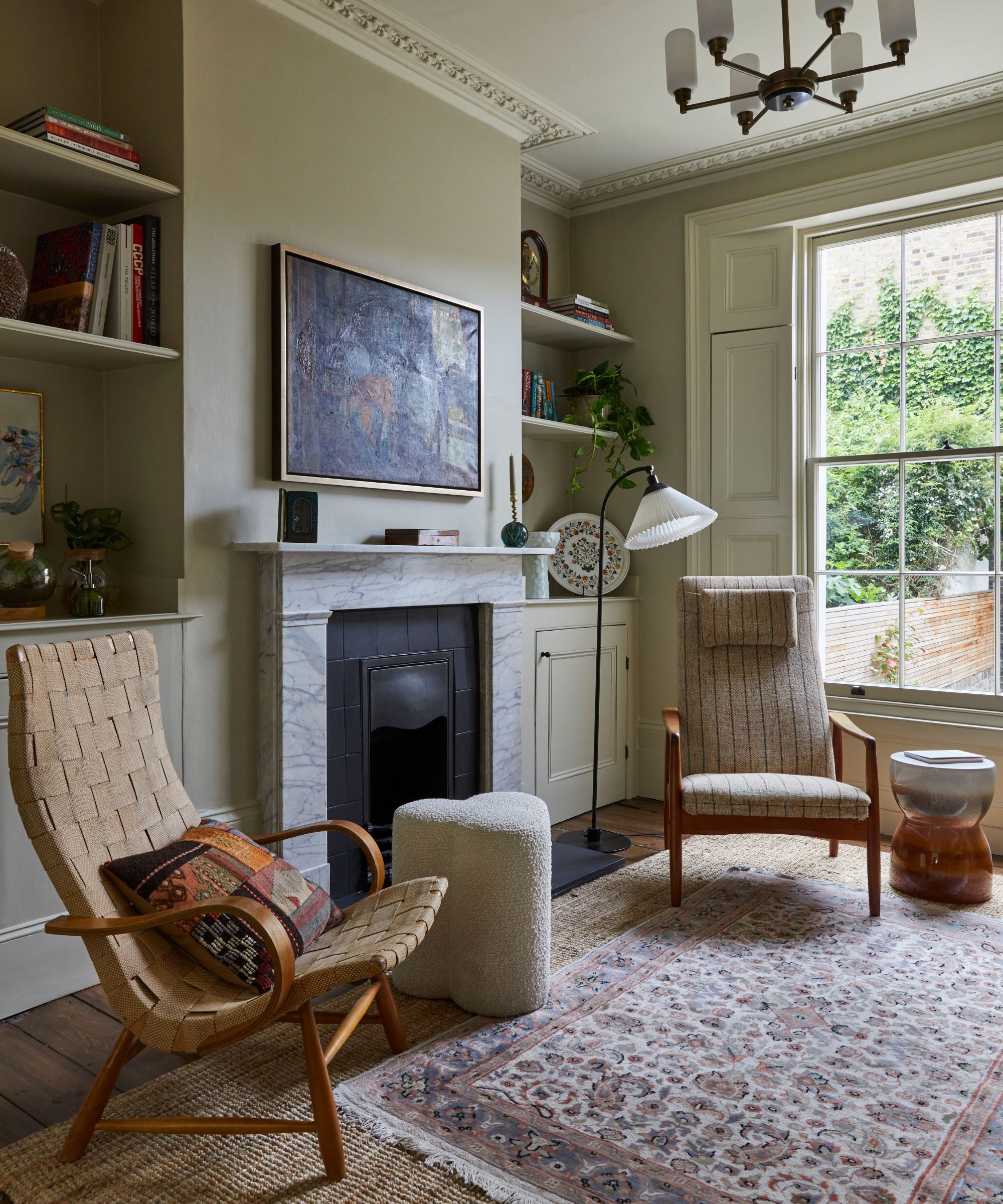 Living room with beige walls, crown molding, large bay window, marble fireplace, bookshelves, and persian rug