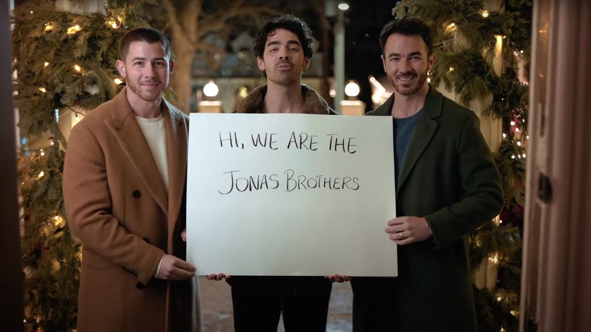 The Jonas Brothers holding a sign introducing themselves in Jonas Brothers Christmas movie promo