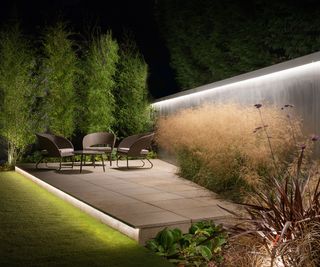 A contemporary patio with a backlit cement wall and ornamental grasses growing