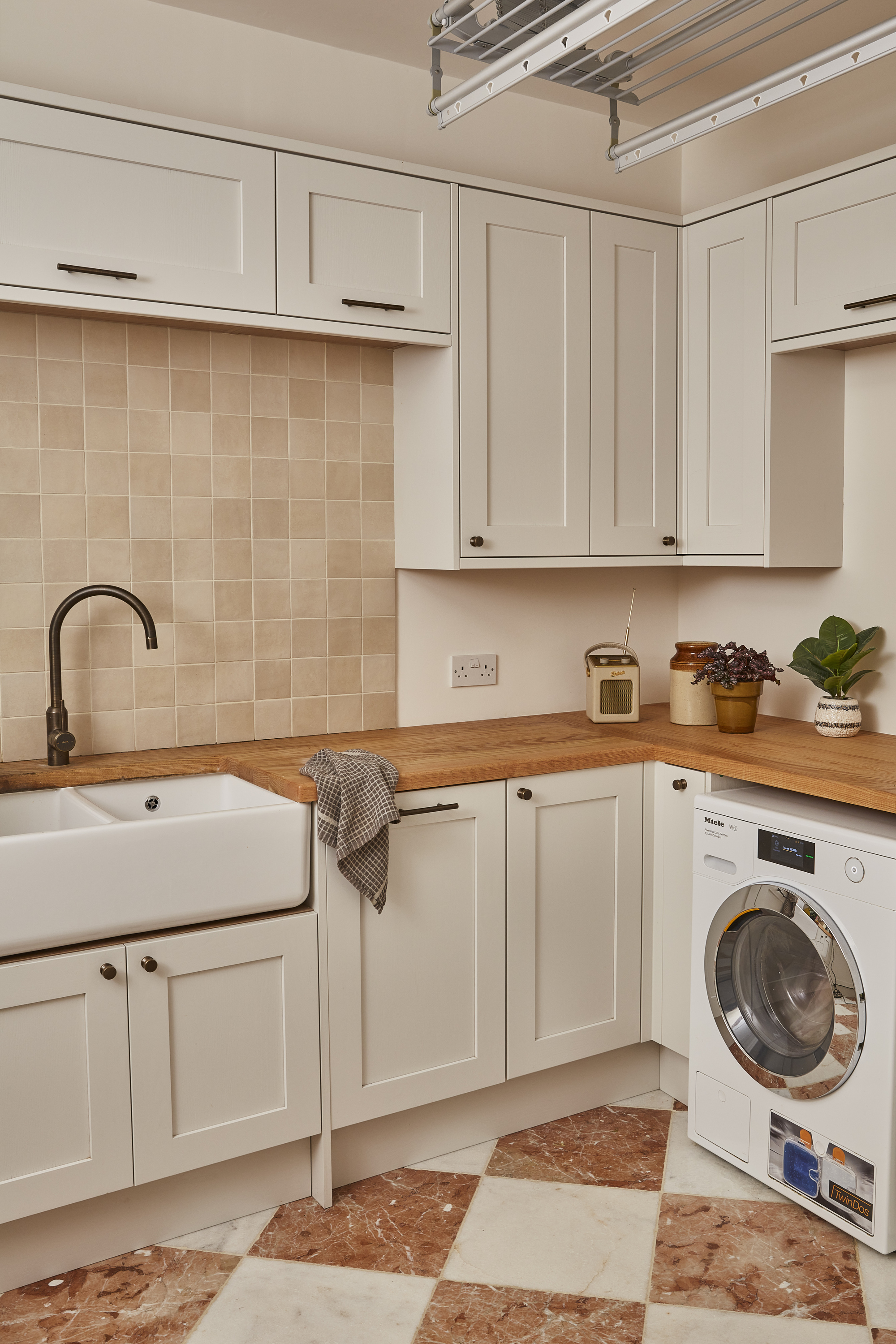 A kitchen with taupe cabinetry, wooden countertops, and white and terracotta colored marble floor tiles in a checkerboard arrangement