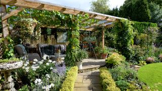 A wooden pergola at the end of a garden with beautiful planting