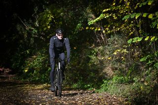 Male cyclist wearing a black Castelli Espresso Air Jacket and Sorpasso Wind Bib Tights riding a Ribble Allroad Ti on a country lane