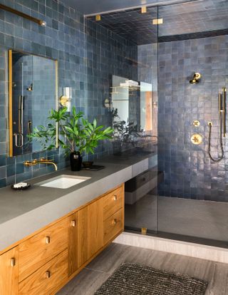 A bathroom with a large shower, blue tiles, and a wooden double vanity