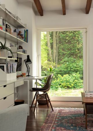 bright home office with large window, white desk and drawers and shelves, a red/purple rug, and wood beamed ceiling