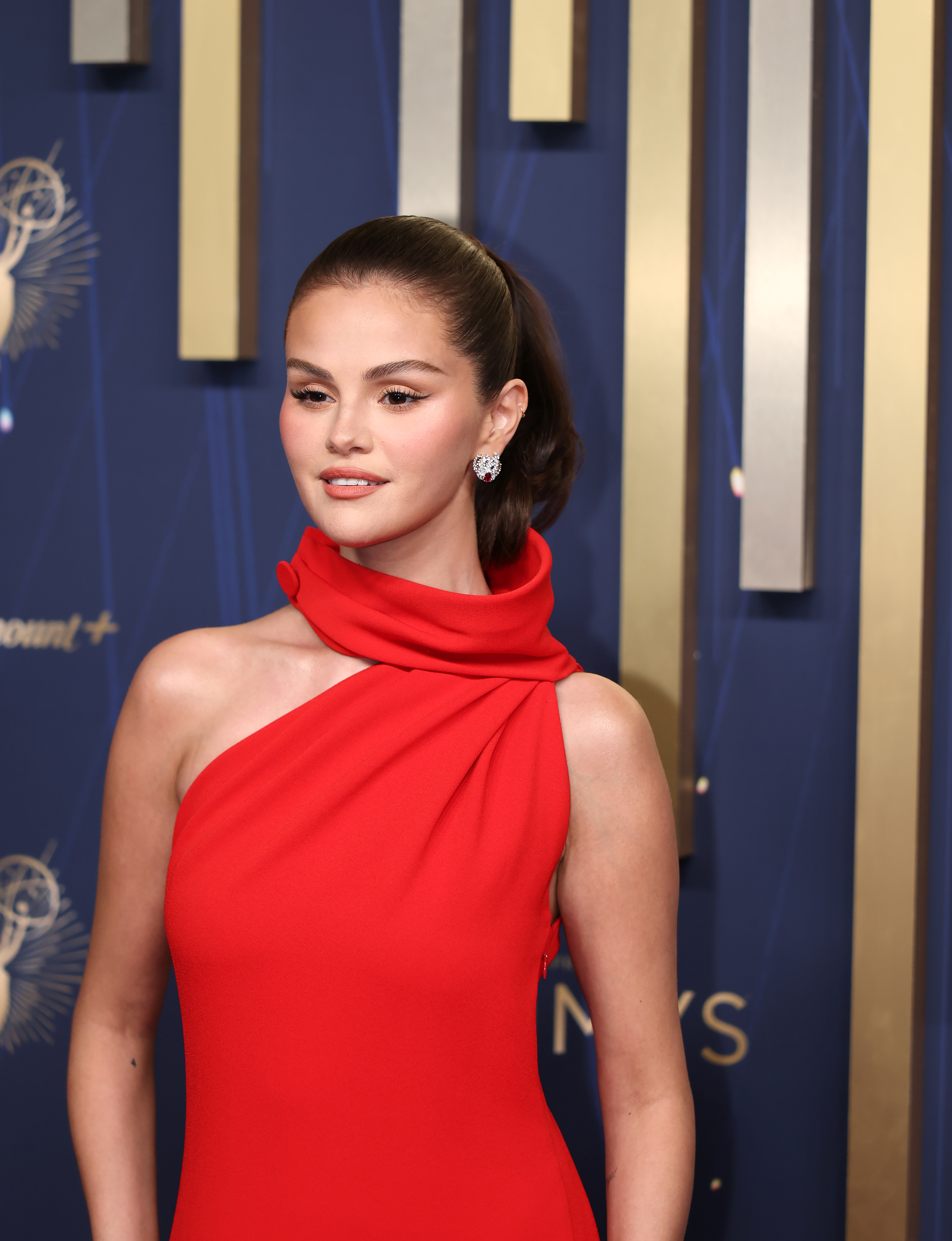 a brunette woman wearing a red, high neck gown and posing on a red carpet