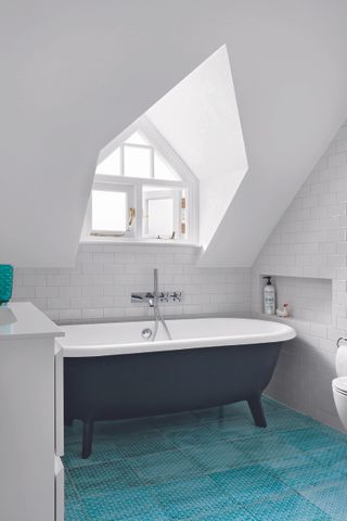 Bathroom with roll top bath and dormer window with turquoise floor tiles and white metro wall tiles.
