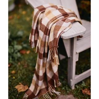 A brown and white chekered wool blanket draped over the edge of a wooden garden chair