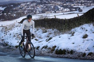 Male cyclist riding up a snowy lane wearing a pale blue jersey