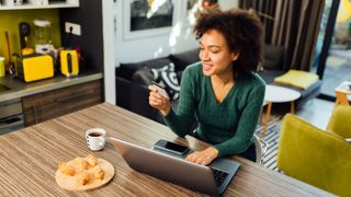 Person using credit card whilst sitting at a desk with a laptop and mobile phone in view