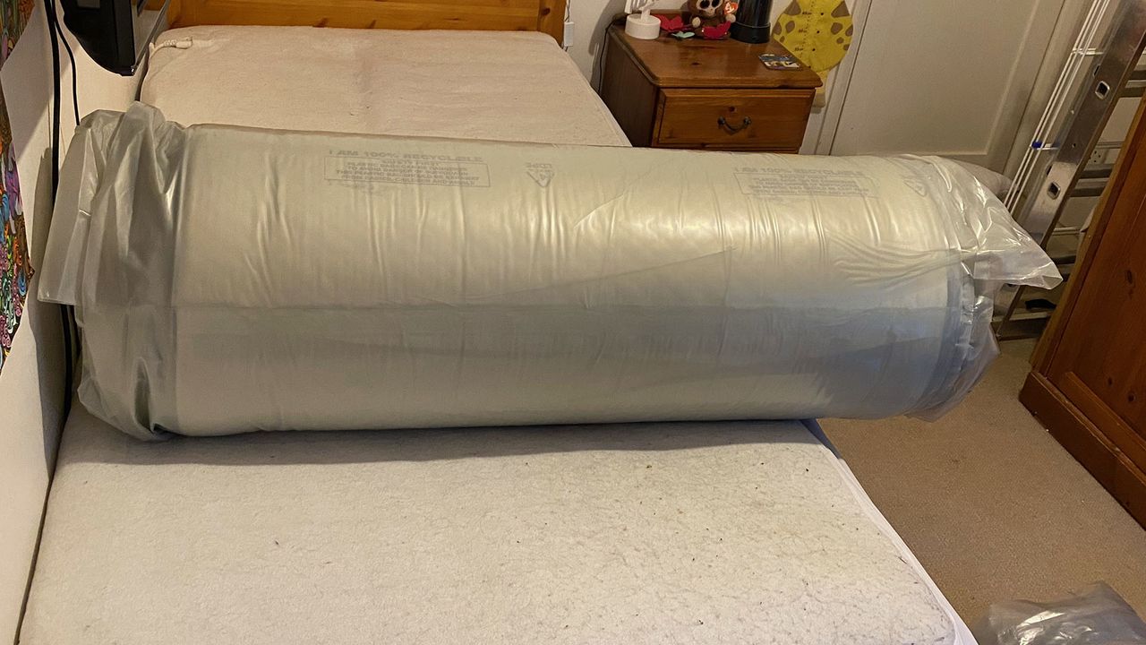 Nectar Essential Hybrid Mattress rolled up in plastic on a bed frame