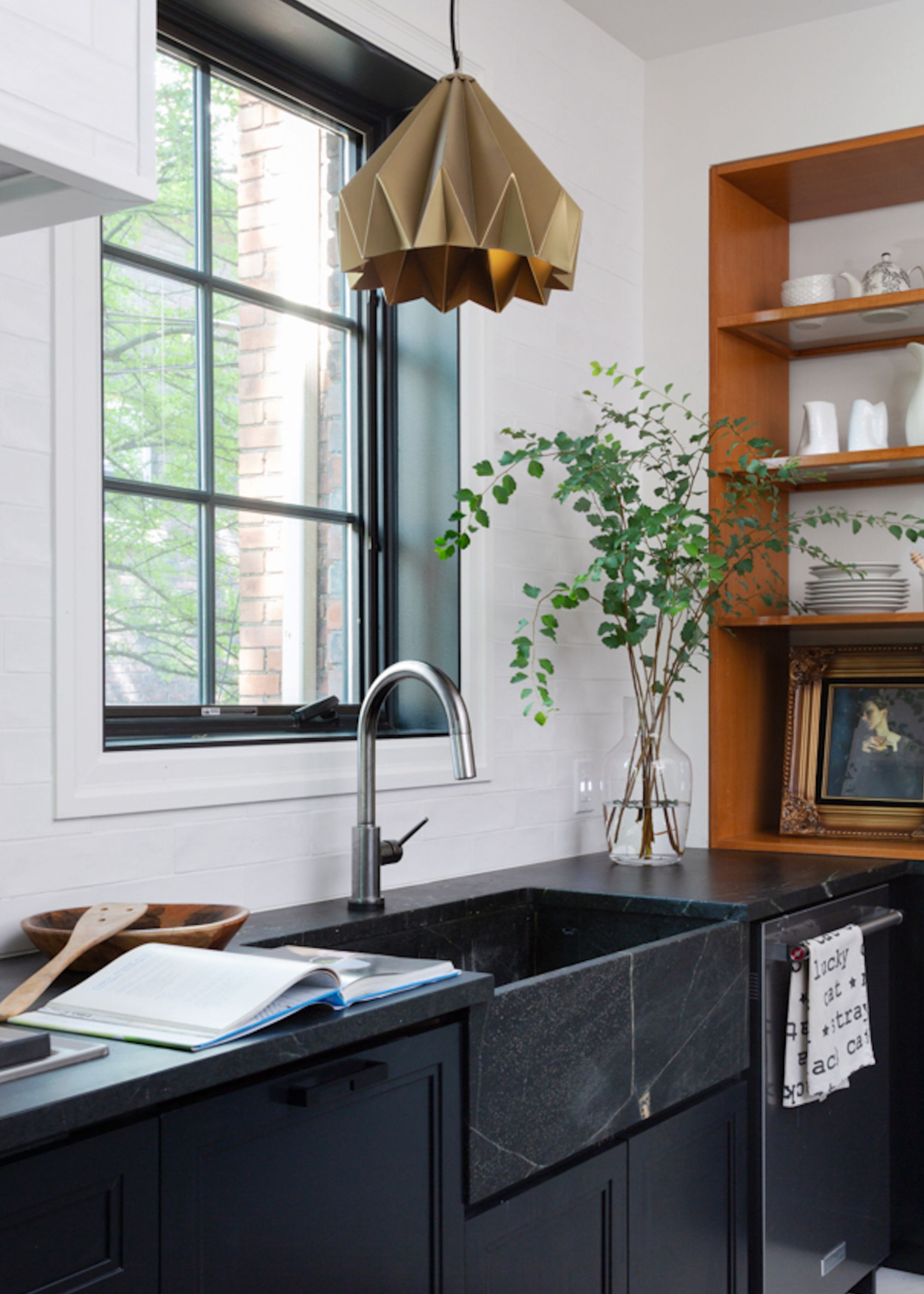 A soapstone kitchen in a contrasting kitchen with shades of white, black and wooden textures used throughout. There is a large brass pendant hanging above the soapstone sink