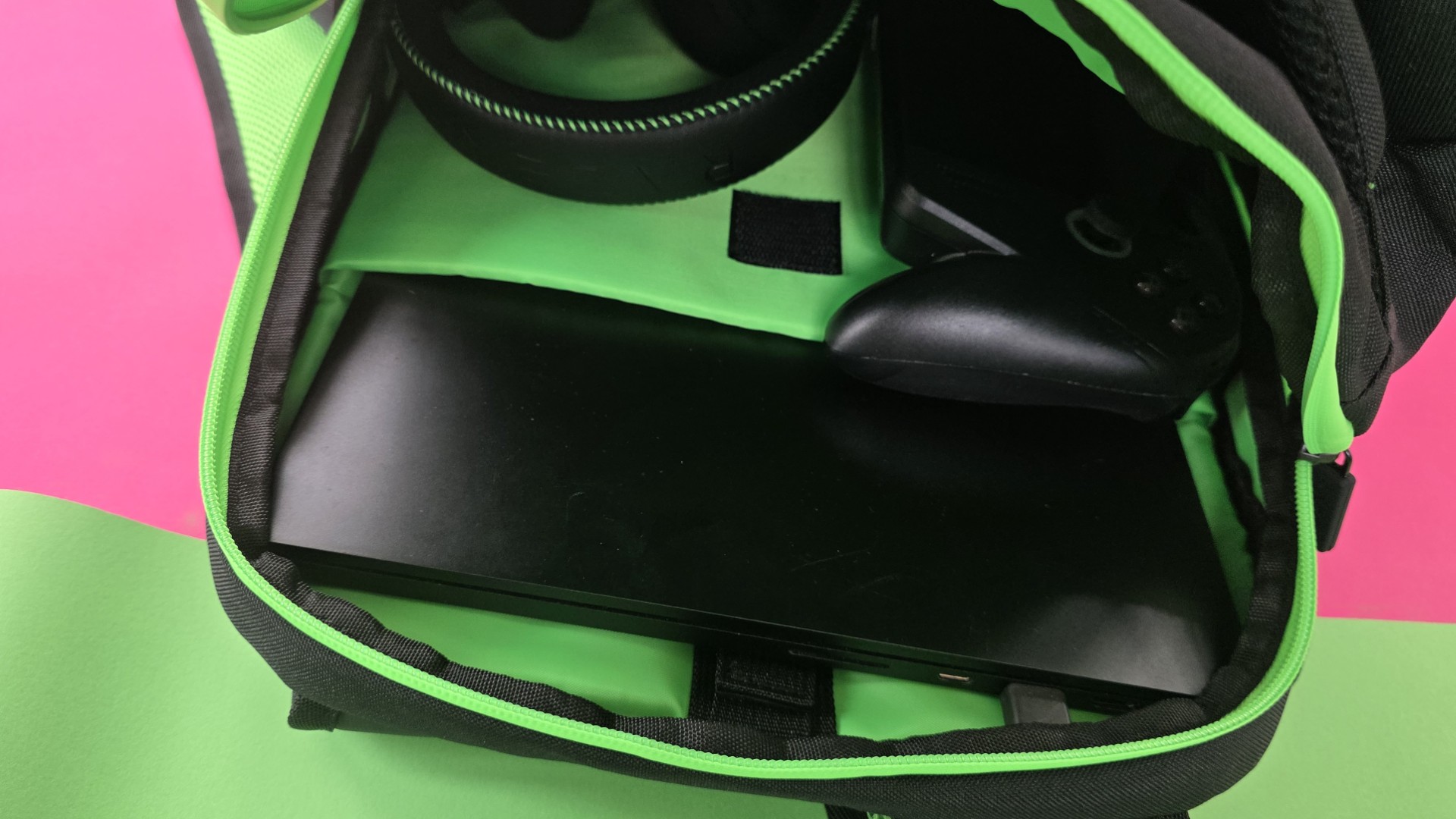 A black Razer backpack, open with laptop, headset and gaming handheld inside