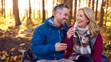 An older couple smile as they take a break while hiking in the woods.