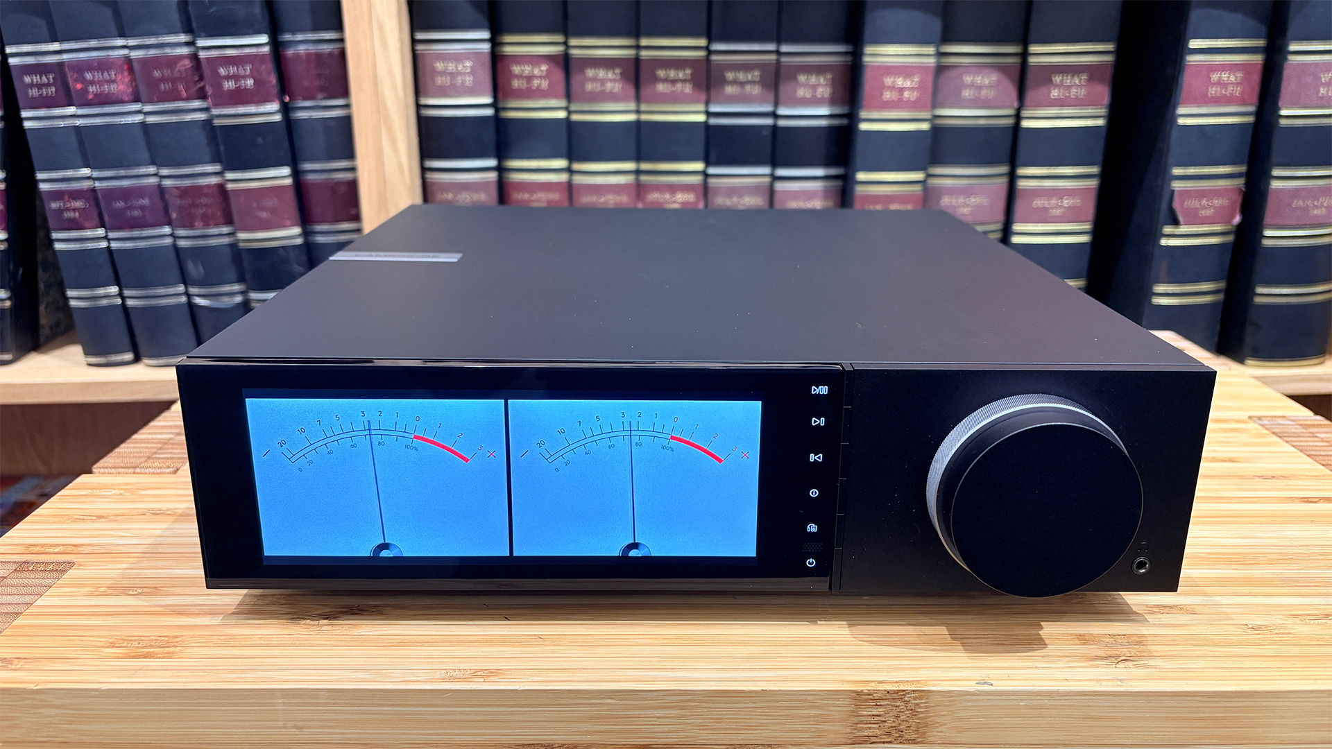 Cambridge Audio Evo 150 SE music streamer on wooden hi-fi rack in front of bookcase with VU meters on display screen