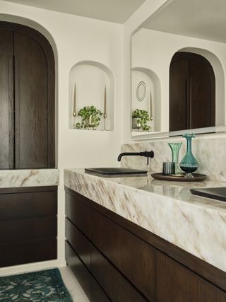 A bathroom with dark wooden cabinetry, a double marble vanity, and black hardware
