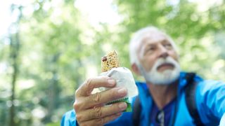 senior man eating a protein bar on a hike