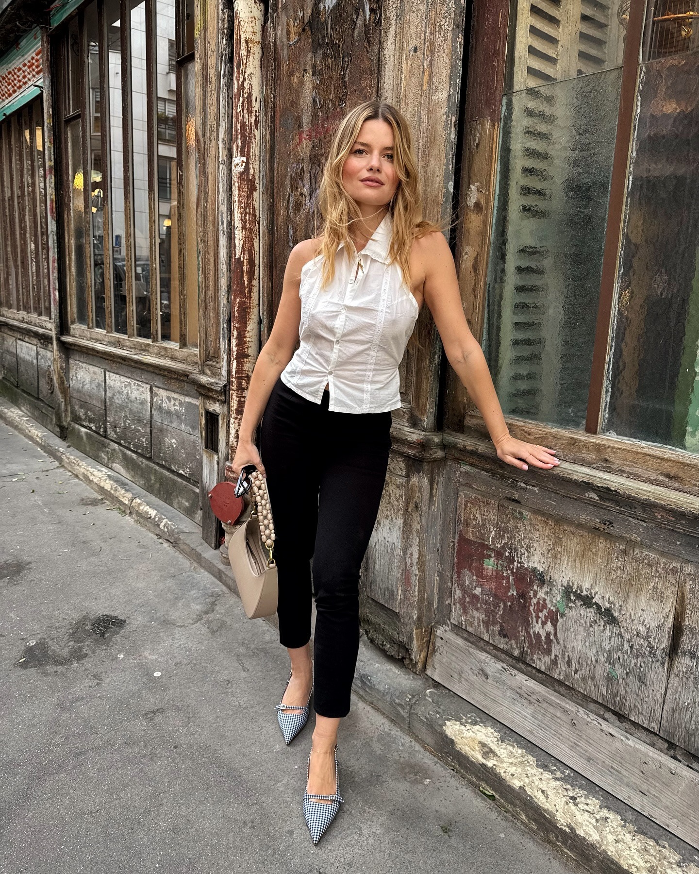 Woman wears black cigarette pants, white vest top and gingham slingback flats.