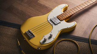 The Squier Classic Vibe Telecaster Bass is a fine-looking four-string in a custard-colored Vintage White, and is here photographed in close-up, against a plain wooden background. It has a single Wide Range humbucker.