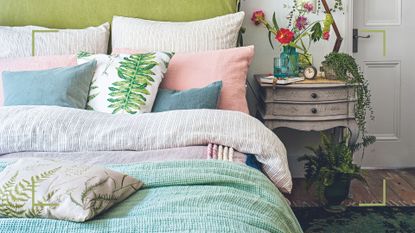 Spring bedroom with lime green fabric headboard striped bedding with flora cushions and bedside table with vase of fresh flowers showing forgotten bedroom item you should be cleaning weekly