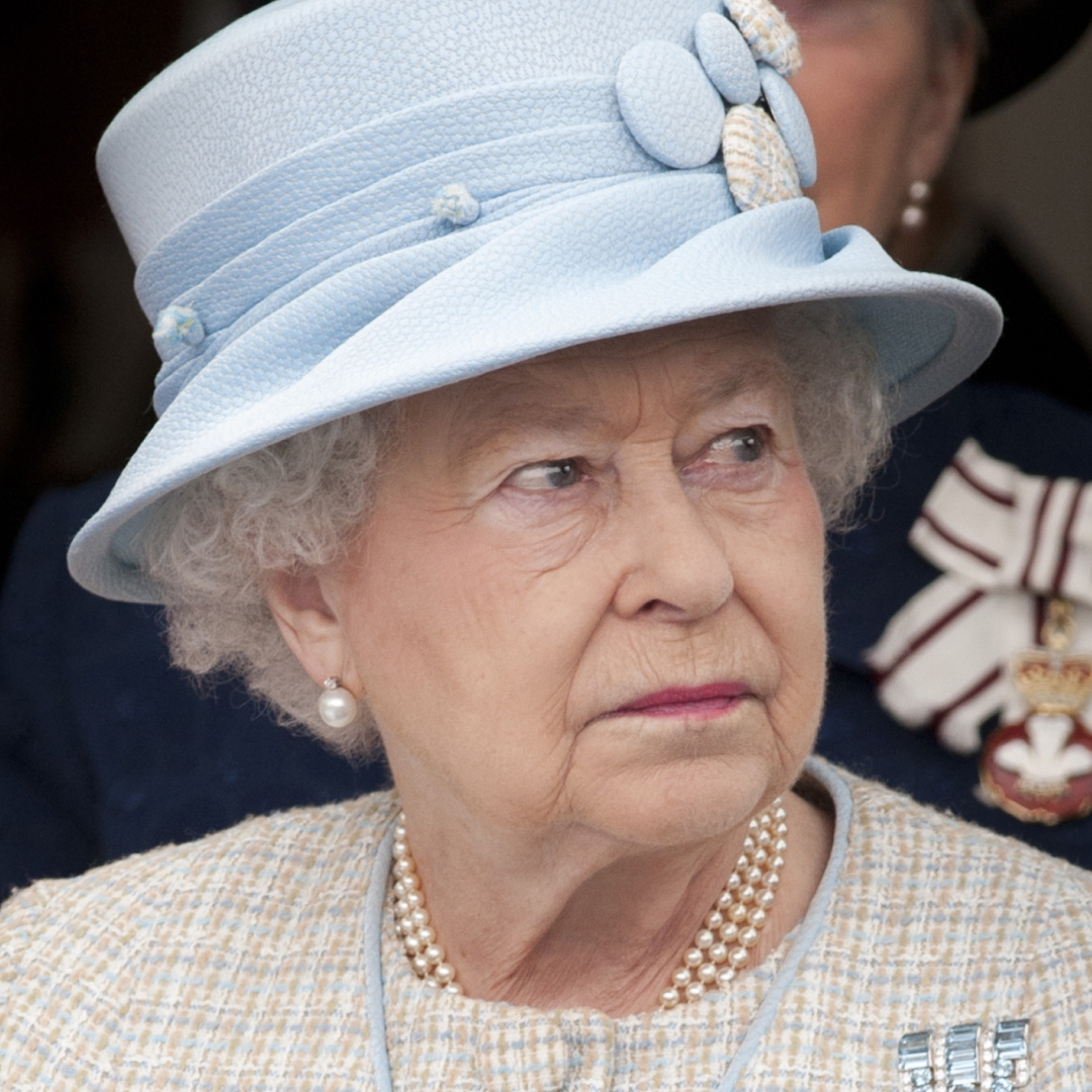 Queen Elizabeth wearing a blue hat and tweed coat with a serious expression