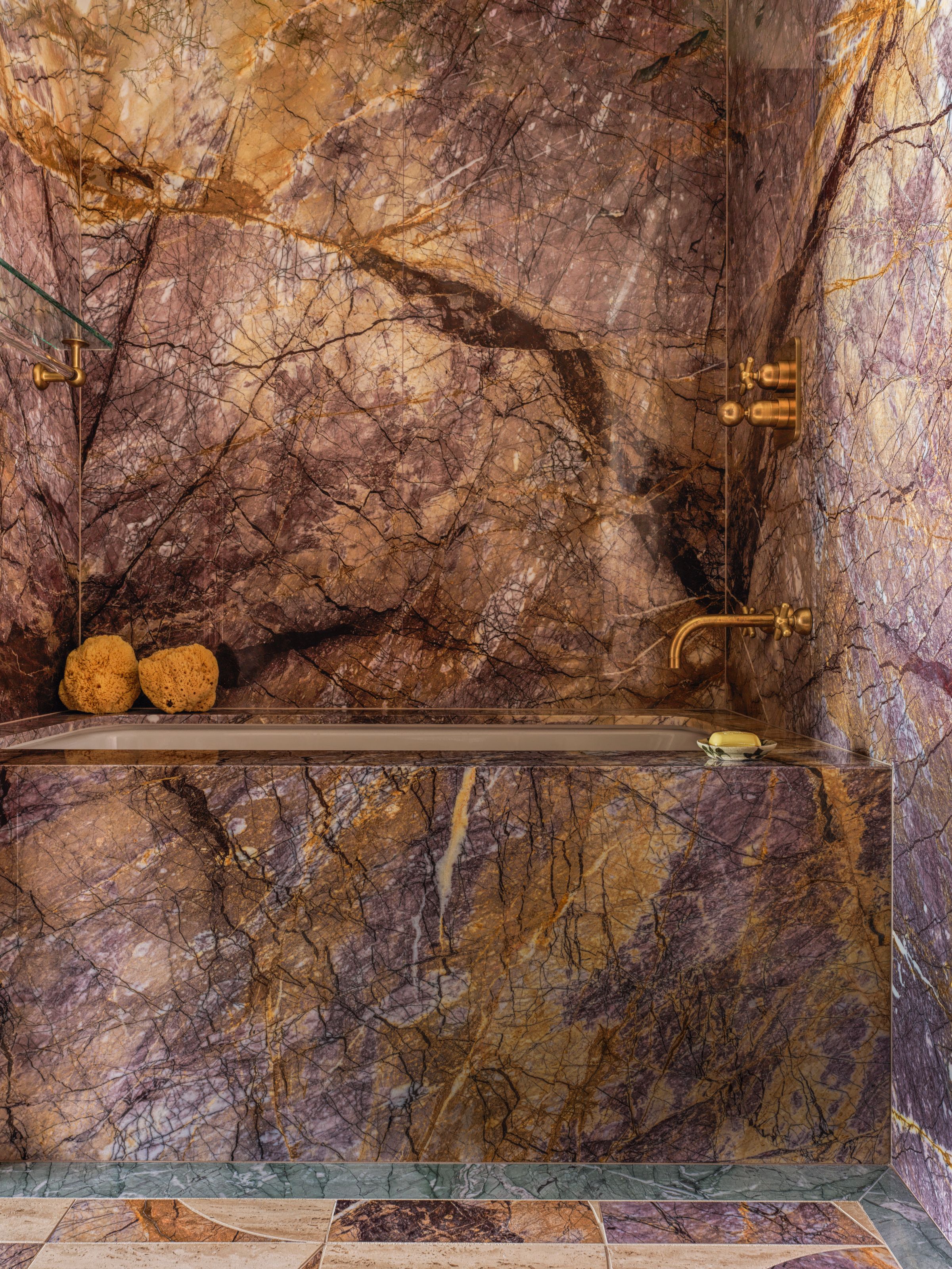 Bathroom with purple and orange stone across the walls and bath, with a blue stone border on the floor