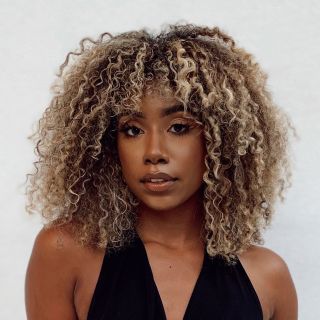 A woman with a naturally curly layered bob and blonde highlights