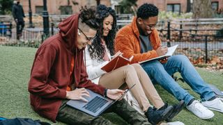Apple student discount: Three students sitting on grass and using laptops