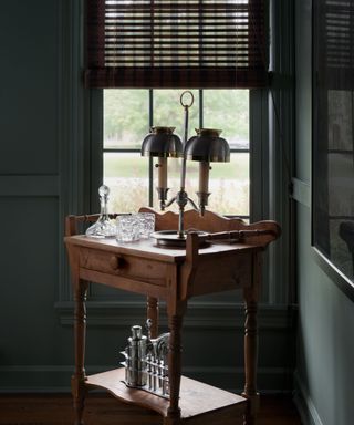 A vintage bar cart in front of a window in a green home library