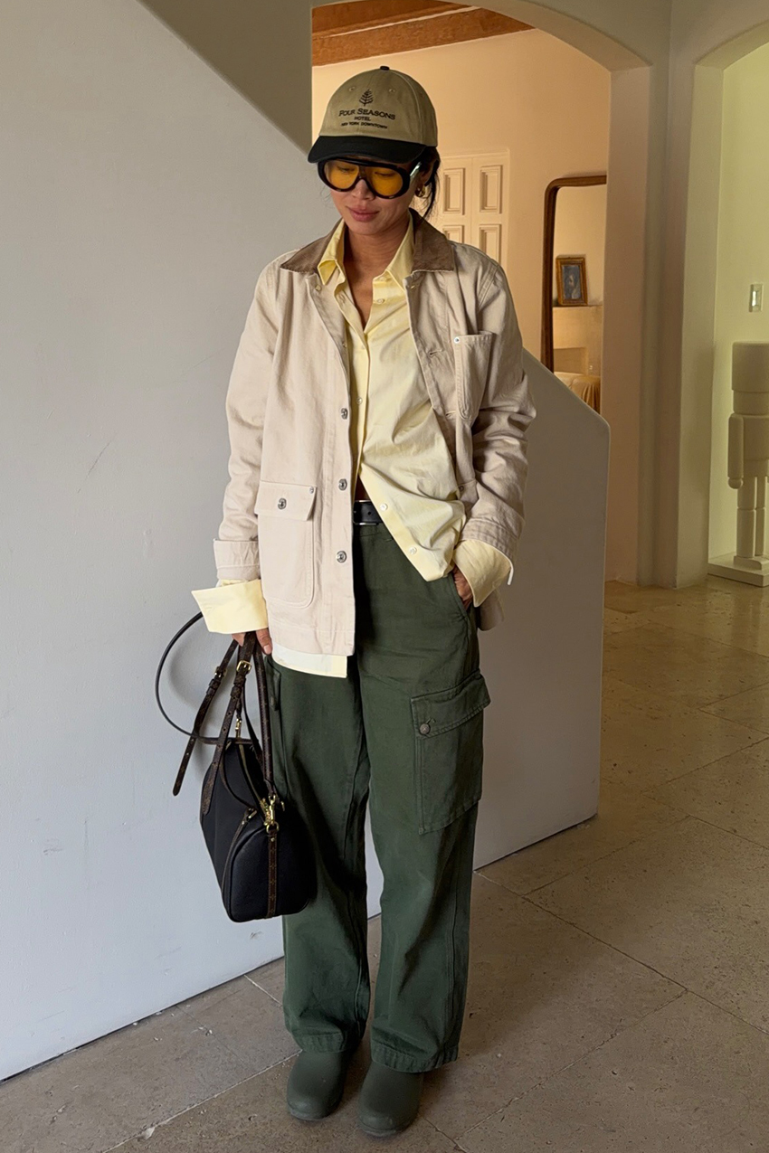 a woman wearing a baseball cap, yellow button-down, green cargo pants, and boots
