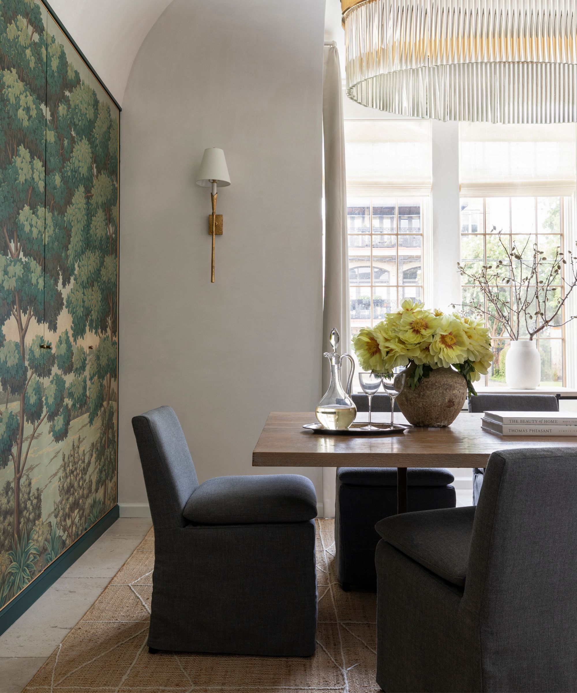 white painted dining room with a large gold and crystal chandelier with a wood table, navy slip covered dining chairs with a large wall tapestry