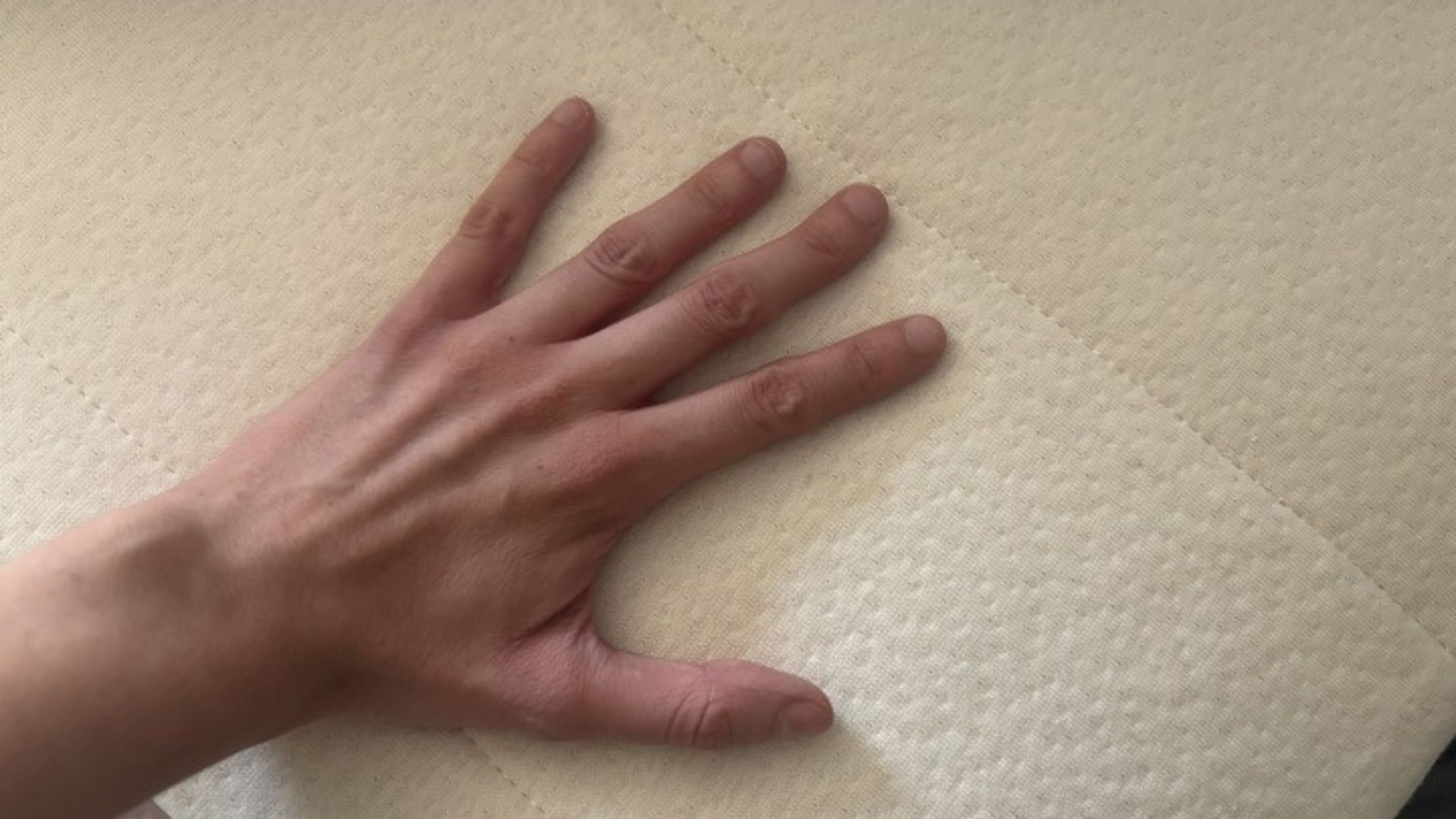 A tester's hand feels the temperature of the Birch Plush Organic Mattress Topper.