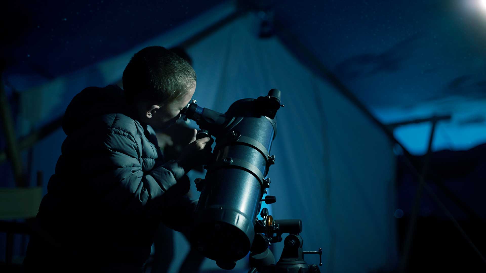The child is using a telescope at night
