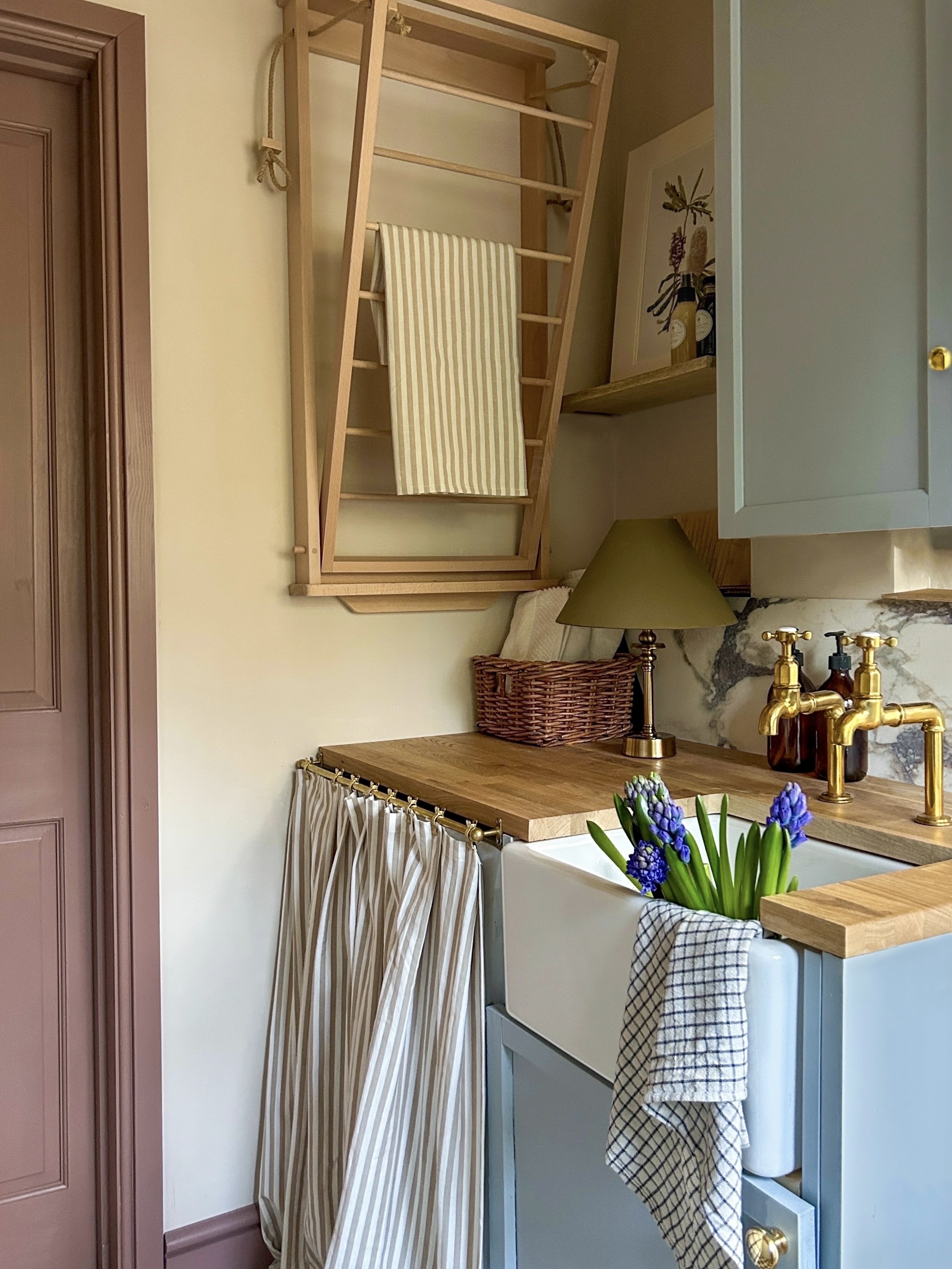 A utility room with a butler sink, light blue cabinetry, and a wooden fold-out drying rack