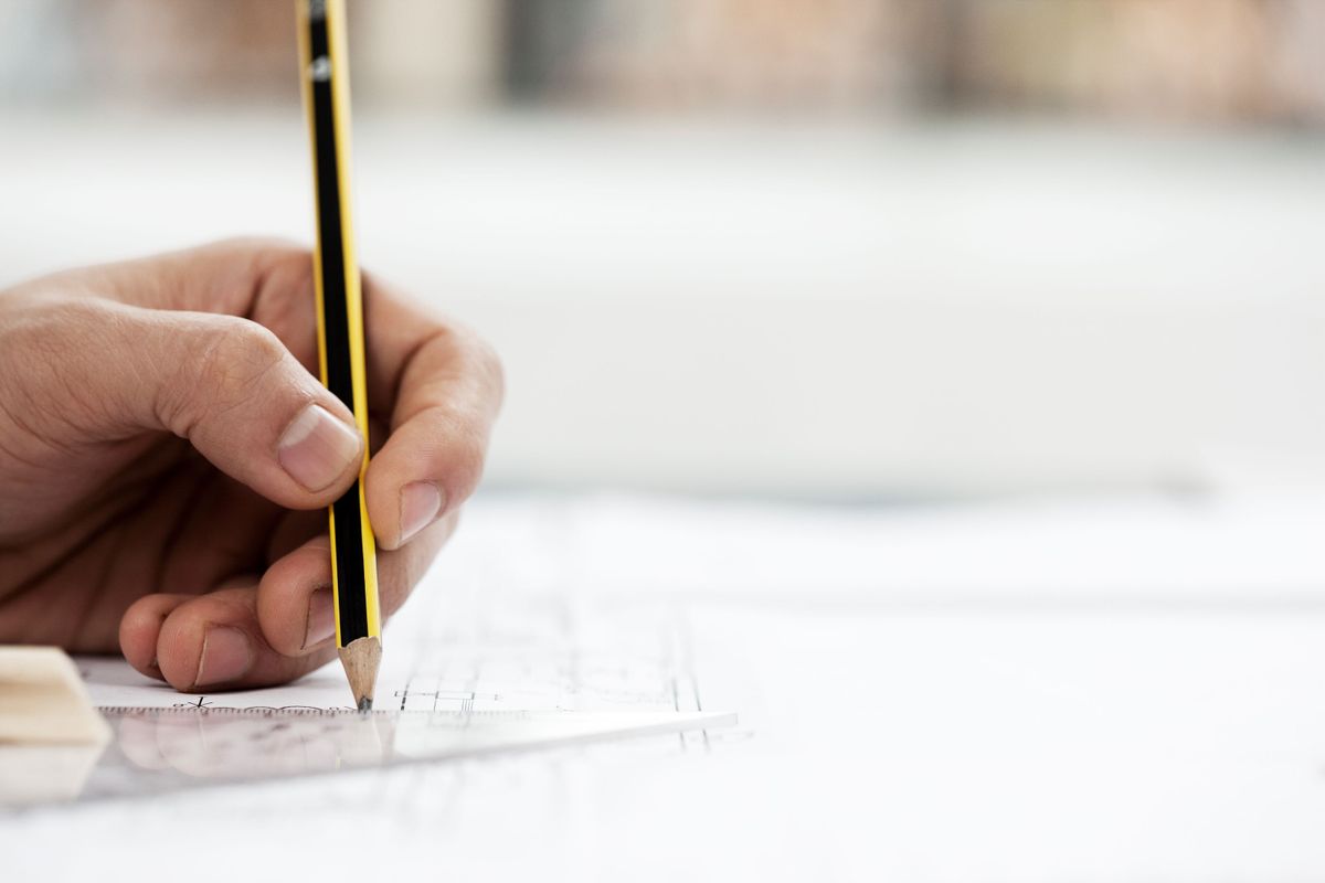 A hand gripping a pencil over building plans