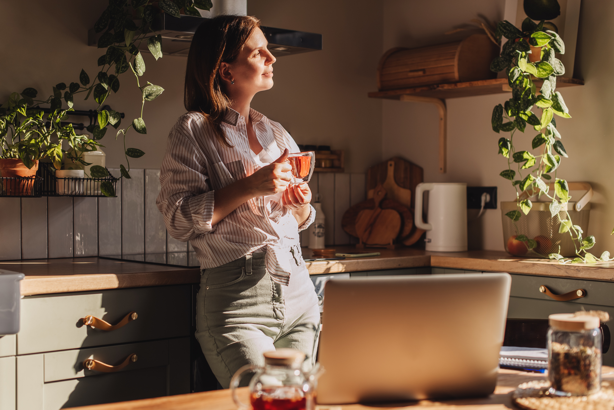 A woman standing in her kitchen happily, while holding a mug of herbal tea.